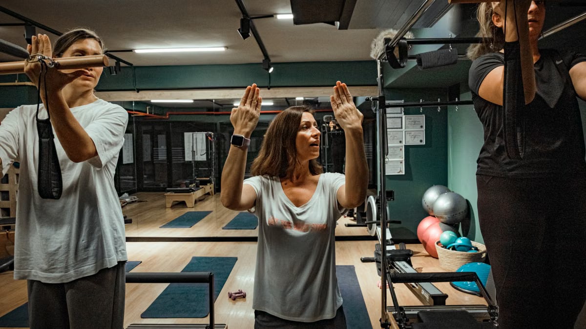 Pilates instructor guiding two women during a workout in a modern gym environment.