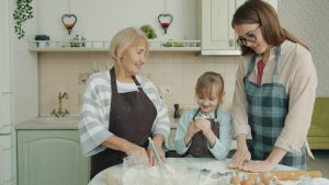 Happy family child, mother and grandmother are cooking baking and talking in kitchen concentrated on bakery. People, apartment and women concept.