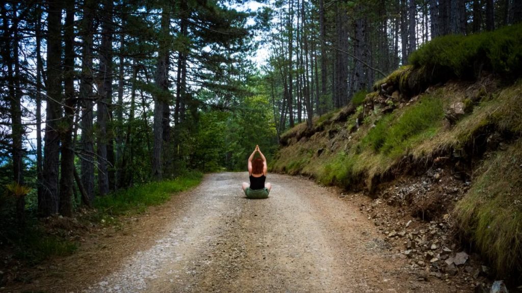 A person meditating on a forest path, embracing nature's tranquility in summer.